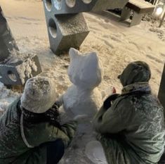 two people building a snowman outside in the snow with one person looking at it