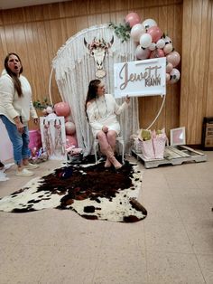 a woman sitting on a chair in front of a cow skin rug and balloon decorations