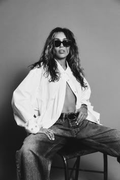 a black and white photo of a woman sitting on top of a chair wearing sunglasses