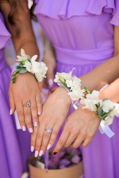 two bridesmaids in purple dresses hold their wedding rings and bouquets over the cake