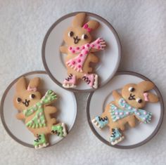 four decorated cookies are on plates on a white tablecloth, one is shaped like a teddy bear and the other is made out of icing