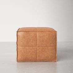 a brown leather ottoman sitting on top of a white floor next to a gray wall