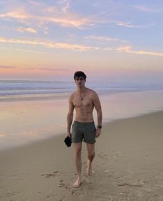 a shirtless man walking on the beach at sunset