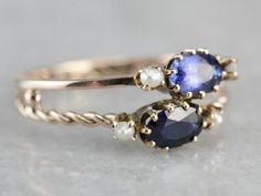 "Two bands, one twisted, one simple and polished have been fused together to create this ready-made stacking set, with oval cut sapphires, one a shade darker than the other, both accented perfectly by creamy white seed pearls, this ring is wonderfully crafted, unique and super sweet! Metal: 10K Yellow Gold Gem: 2 Sapphires totaling 1.11 Carats Gem Measurements: 6 x 4 mm, Oval Accents: 4 Seed Pearls Ring Size: 8.25 Marks: \"10K\" Stamped on the inside band SKU #: U52URV7Y Each piece has been iden Formal Oval Sapphire Stackable Ring, Classic Oval Sapphire Stackable Ring, Pearl Sapphire Ring, Oval Jewelry With A Modern Twist For Weddings, Classic Oval Stackable Sapphire Ring, Anniversary Sapphire Stackable Rings In Oval Shape, Anniversary Sapphire Stackable Rings With Oval Shape, Anniversary Oval Sapphire Stackable Rings, Modern Twist Oval Wedding Jewelry