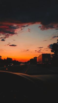 the sun is setting behind some clouds in the sky over a road with cars driving on it