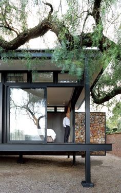 a man standing in the doorway of a small house with trees growing on top of it