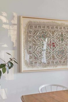 a painting hanging on the wall next to a table with chairs and a potted plant