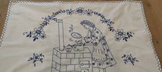 an embroidered tablecloth with a woman cooking on the stove and flowers around her neck