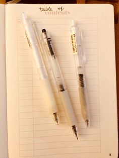 two pens sitting on top of an open notebook