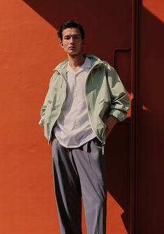 a man standing in front of an orange wall with his hands on his hips and looking at the camera