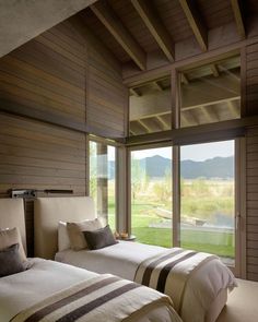 two beds in a room with wooden walls and floor to ceiling windows that look out onto the mountains