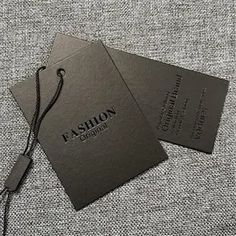 two black business cards sitting on top of a gray cloth covered surface with a lanyard