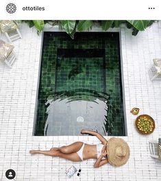 a woman laying on the ground in front of a pool with green tiles and plants