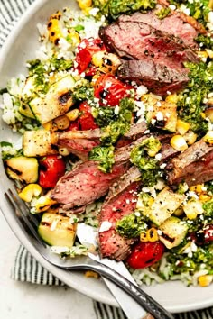 a white plate topped with steak, broccoli and other vegetables next to a fork