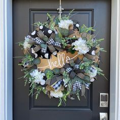 a wreath with the word hello on it hanging from a front door, decorated with flowers and greenery