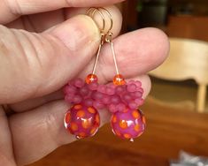 a pair of pink and orange beaded earrings in the palm of someone's hand