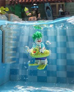 a lego figure floating in the water near a swimming pool with other toys on it