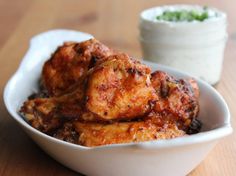 a white bowl filled with chicken wings next to a small container of ranch dressing on a wooden table