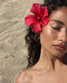 a woman with her eyes closed and a flower in her hair on the sand at the beach