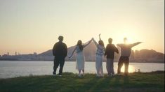 four people standing in front of a body of water with their arms up and hands raised