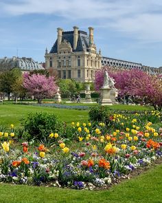 a large building with lots of flowers in the foreground and green grass around it