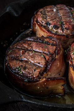 four steaks cooking in a skillet on top of a wooden table with herbs