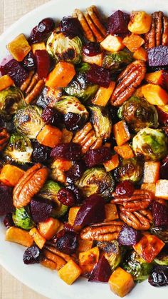 a white plate topped with roasted vegetables and pecans on top of a wooden table