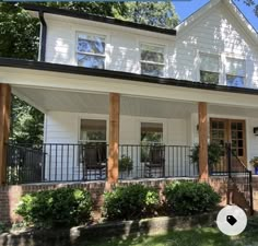 a white two story house with black railings and trees in the front yard on a sunny day