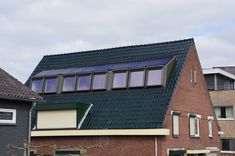 a house with a solar panel on the roof and windows above it is surrounded by other houses