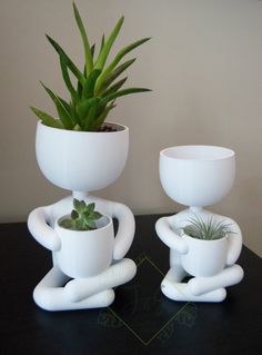 two white planters sitting on top of a black table next to a potted plant