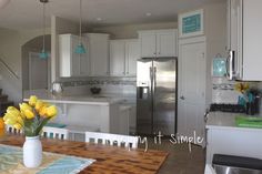 a kitchen with white cabinets and yellow flowers in a vase on the dining room table