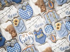 decorated cookies with blue and white designs are arranged on a tablecloth that says it's a boy