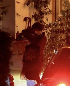 a man standing in front of a sink next to a tree and parked cars at night