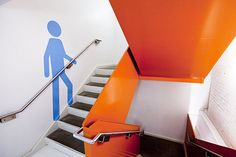 an orange and blue stair case next to a white wall with a man painted on it