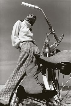 a woman standing next to an old fashioned bicycle on the beach in front of the ocean