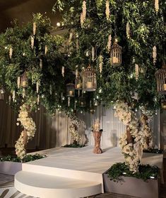 a wedding setup with white flowers and birdcages hanging from the ceiling, surrounded by greenery