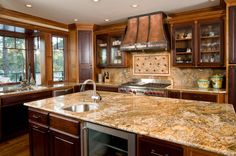 a large kitchen with wooden cabinets and marble counter tops, an oven hood over the stove