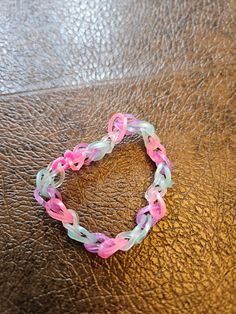 a pink and white bracelet sitting on top of a brown leather table next to a cell phone