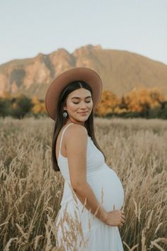 a pregnant woman wearing a brown hat standing in tall grass