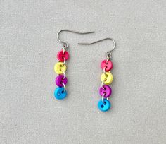 two pairs of earrings with colorful beads hanging from the end of each earring on a gray surface