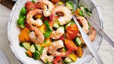 a white bowl filled with shrimp and veggies next to silverware on top of a table