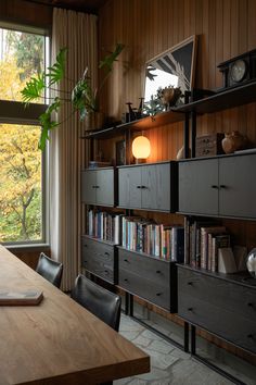 a wooden table sitting in front of a window next to a book shelf filled with books