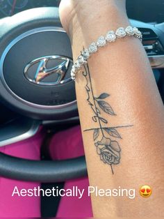 a woman's arm with a rose tattoo on it and a steering wheel behind her