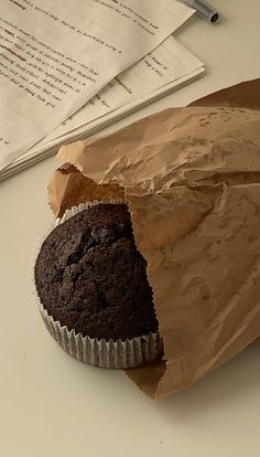 a chocolate muffin in a wrapper sitting on top of a table next to some papers