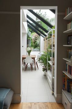 an open door leading to a dining room with bookshelves and plants in it