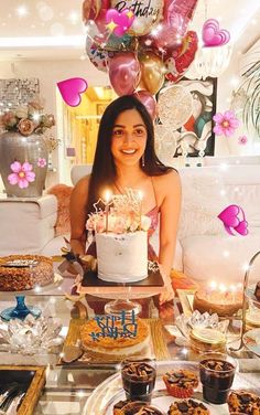 a woman sitting in front of a table filled with cakes and desserts