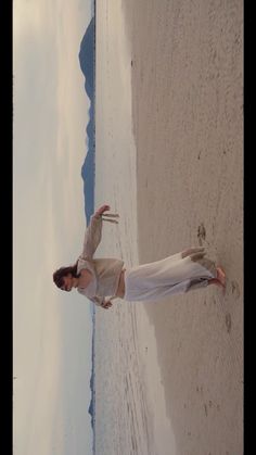 a woman standing on top of a sandy beach next to the ocean with her arms in the air