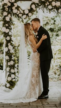 a bride and groom kissing under an arch decorated with flowers