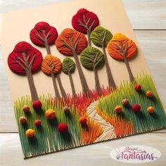 a card with trees made out of yarn on top of grass and red balls in the middle