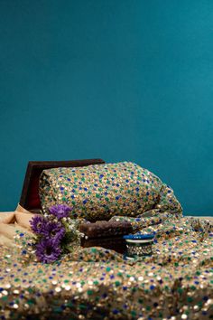 a bed covered in gold sequins with a purple flower on the pillow next to it